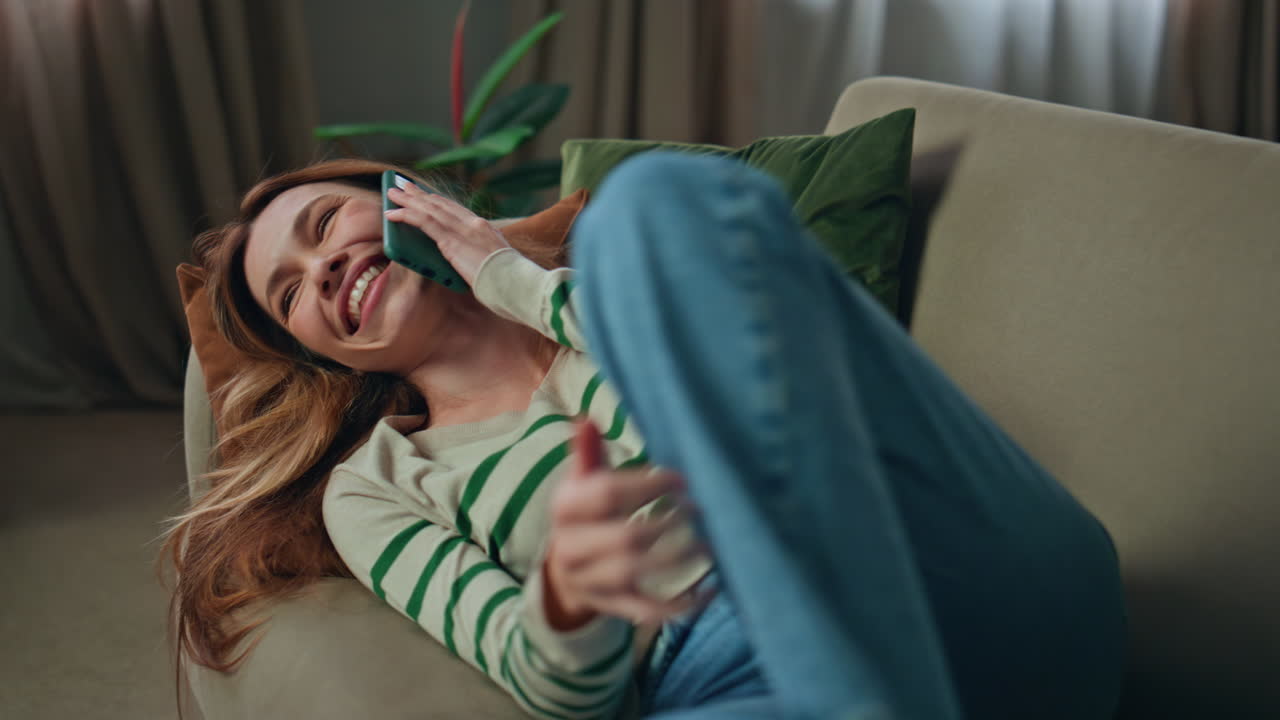 Smiling lady calling cellphone sharing news at home couch. Happy woman talking