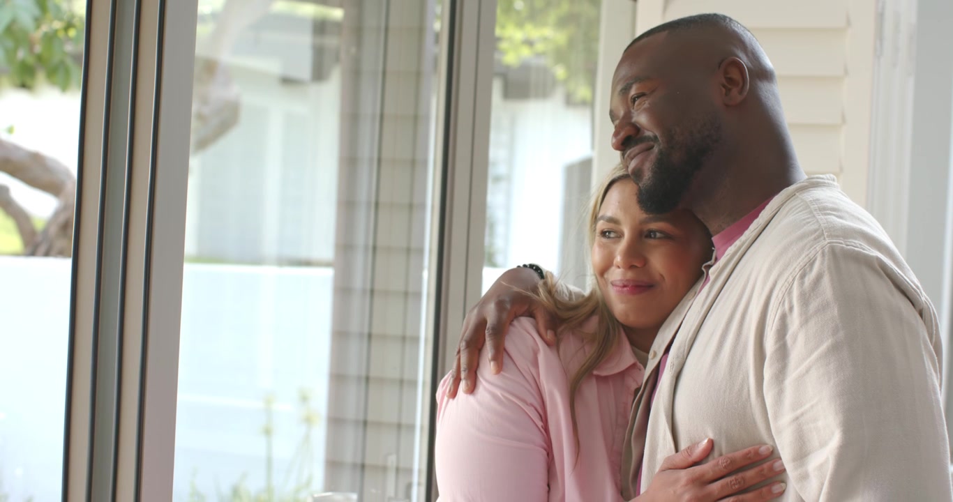 African American couple standing at home by window, man placing arm, couple gazing out, copy space