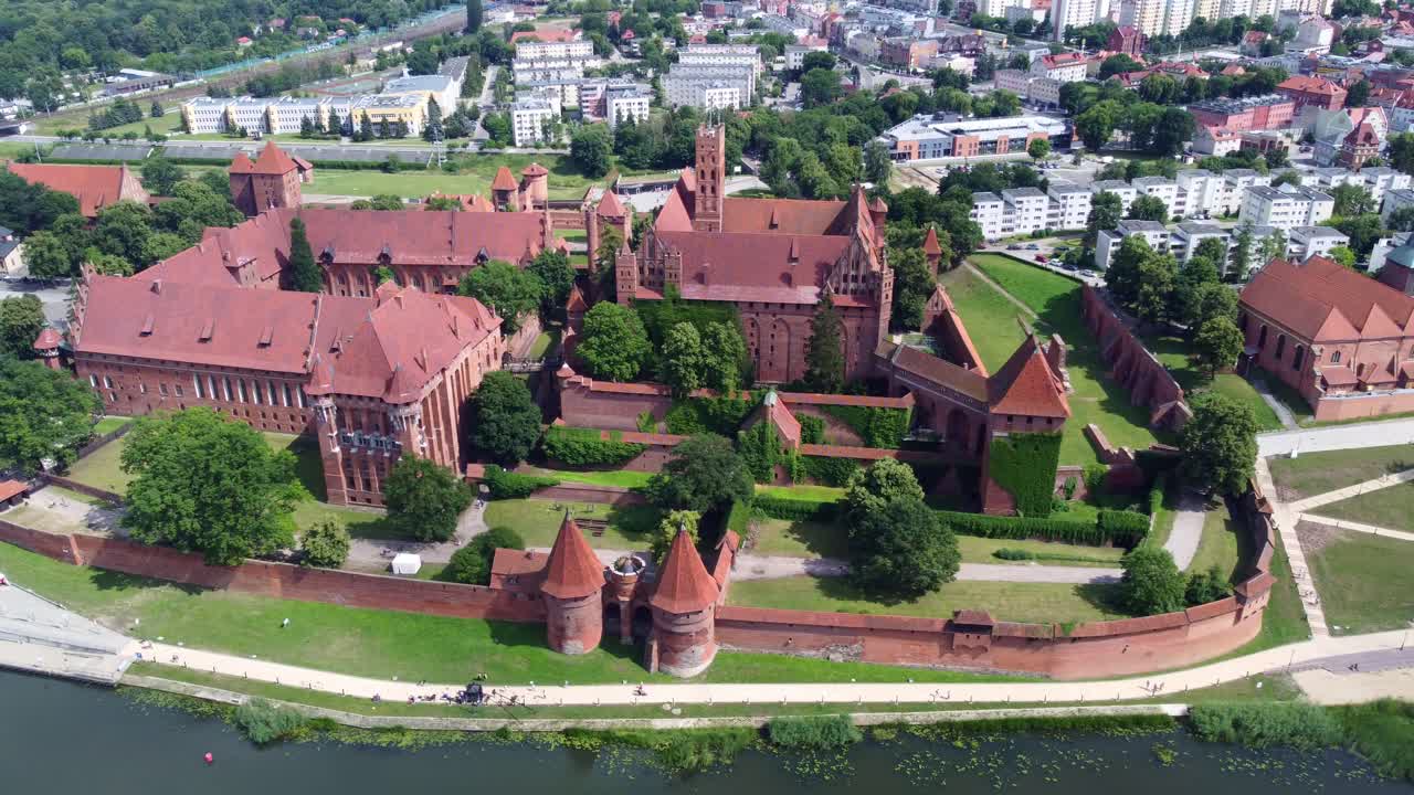 Aerial tracking left across Malbork Castle in Poland, a medieval fortress and UNESCO listed historical site by the river water