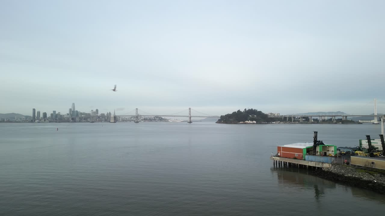 A slow aerial zoom in of the Port of Oakland and the San Francisco Bay Bridge in the distance.