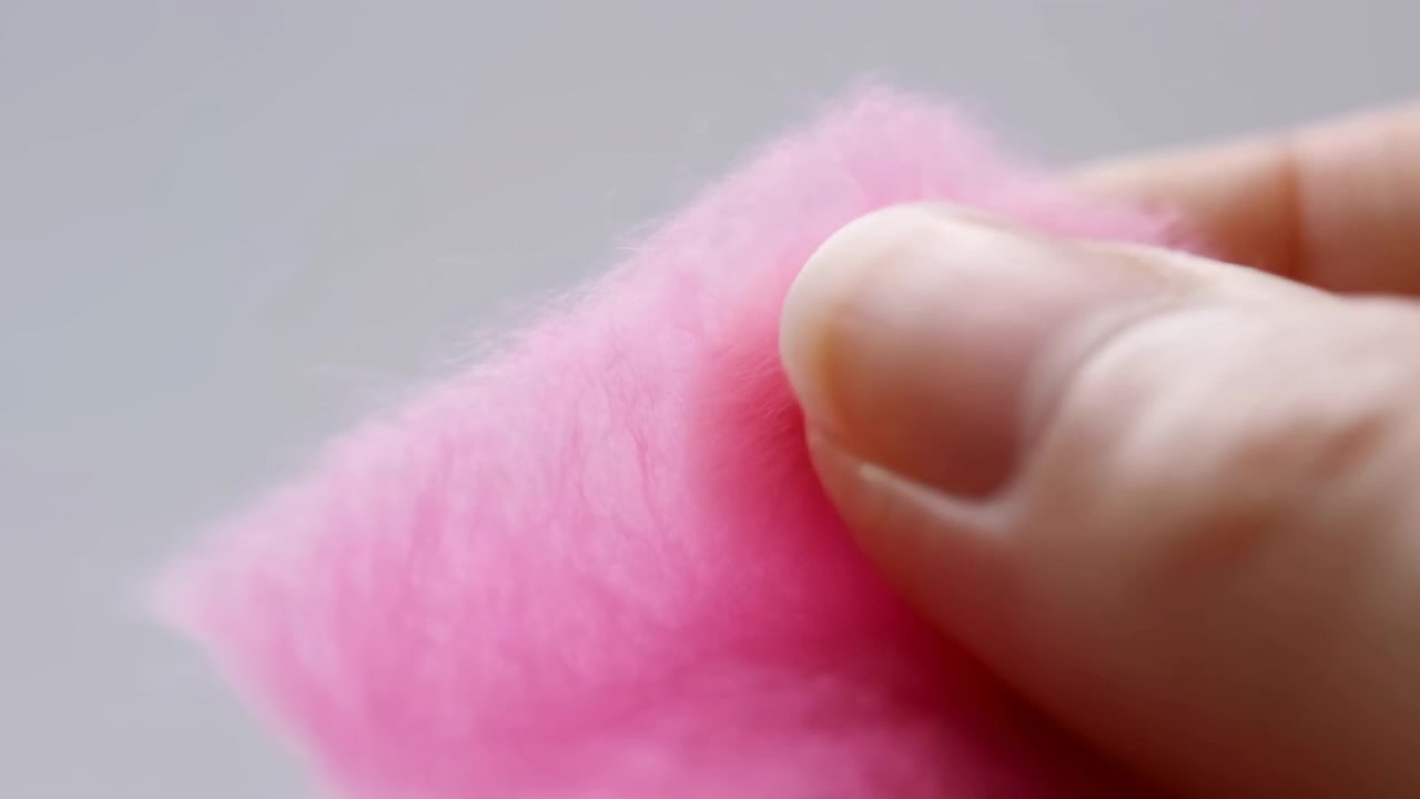 Intimate macro closeup of thumb and fingernail pinching soft pastel pink plush fabric, showing visible compression, fuzzy texture, gentle skin detail, soft
