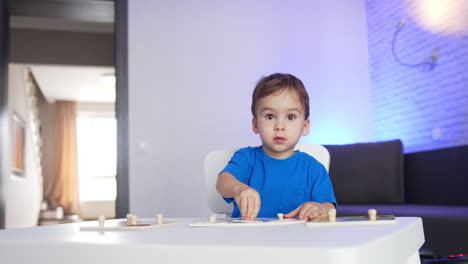 beautiful toddler boy in blue t-shirt plays at desk at home. kid finishes his game and stands up.