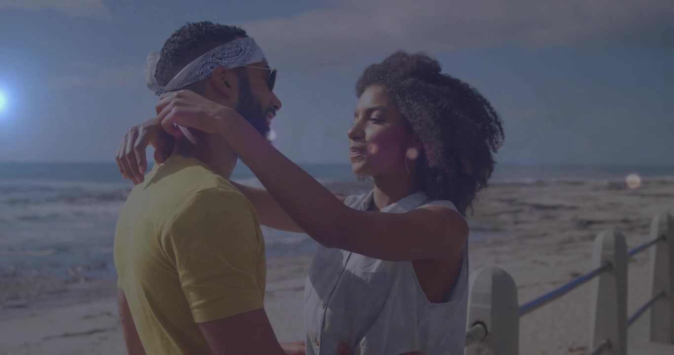 lifestyle couple on beachfront railing while woman speaking, reaching, untying bandana for styling