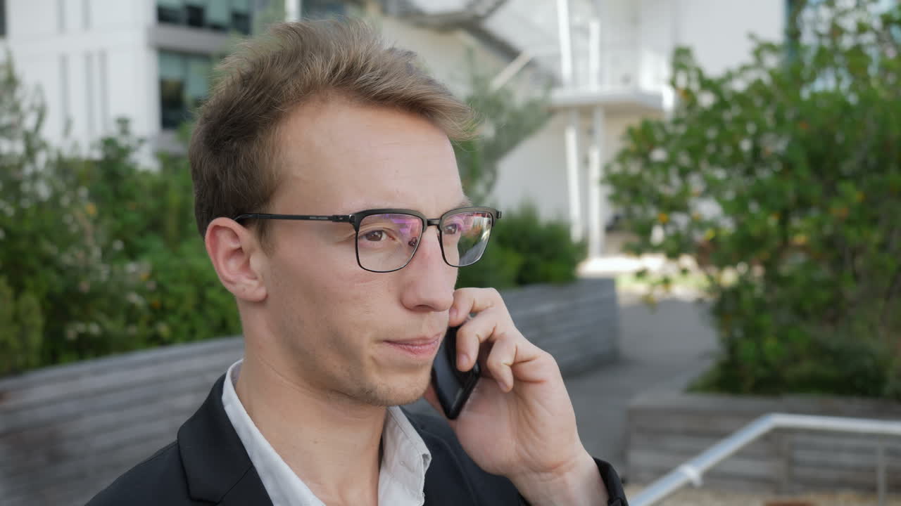 심각한 백인 남자가 밖에서 전화로 이야기하고 협상하고 있습니다.