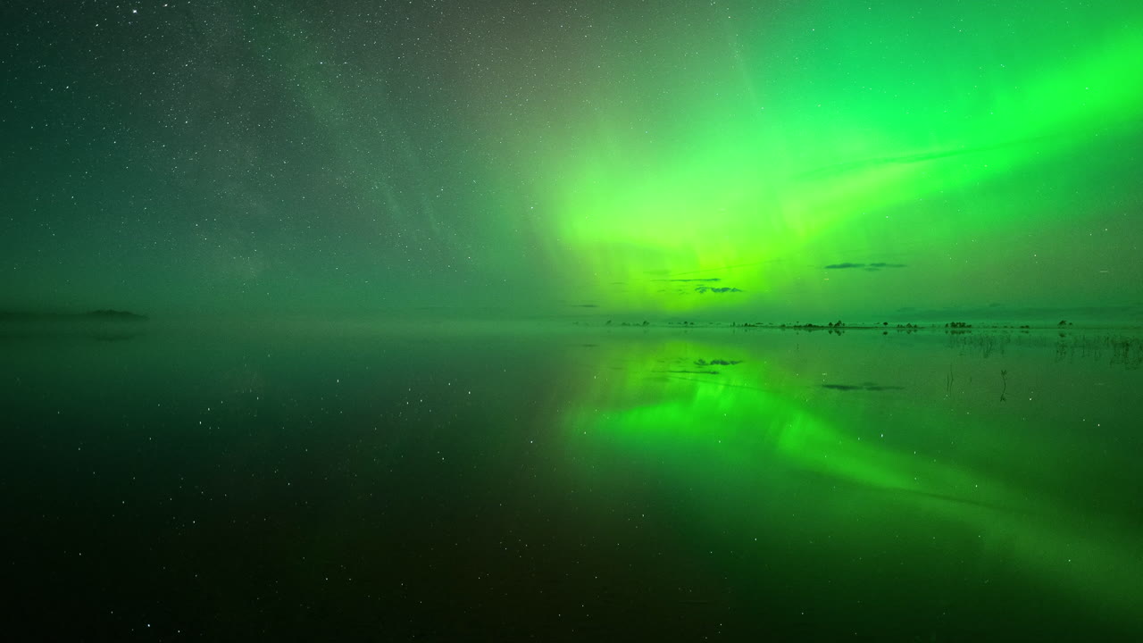 Northern lights glowing green auroras reflecting off a calm lake at night in Estonia, half green light and half starry sky as it spreads