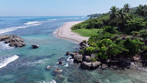 Aerial-forward-flight-over-rocky-coastline-with-sandy-beach-and-tropical-green-scenery-at-sunny-day---Playa-Quemaito,-Barahona