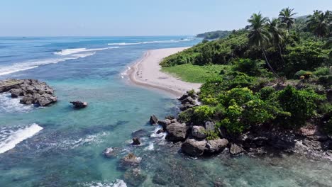 aerial forward flight over rocky coastline with sandy beach and tropical green scenery at sunny day - playa quemaito, barahona