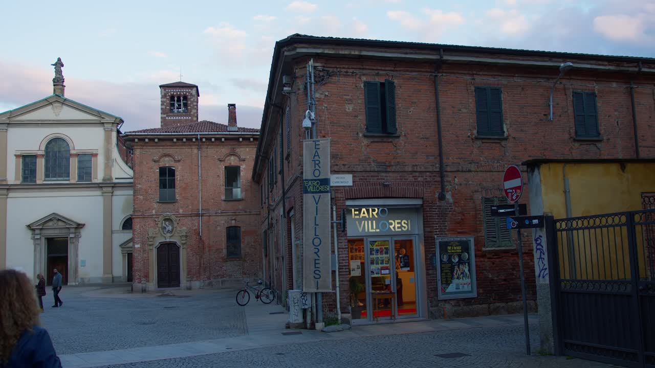 A slow-motion wide shot of Teatro Villoresi and a cathedral in Monza, Italy, under blue moonlight, evoking a cold, mystical atmosphere.