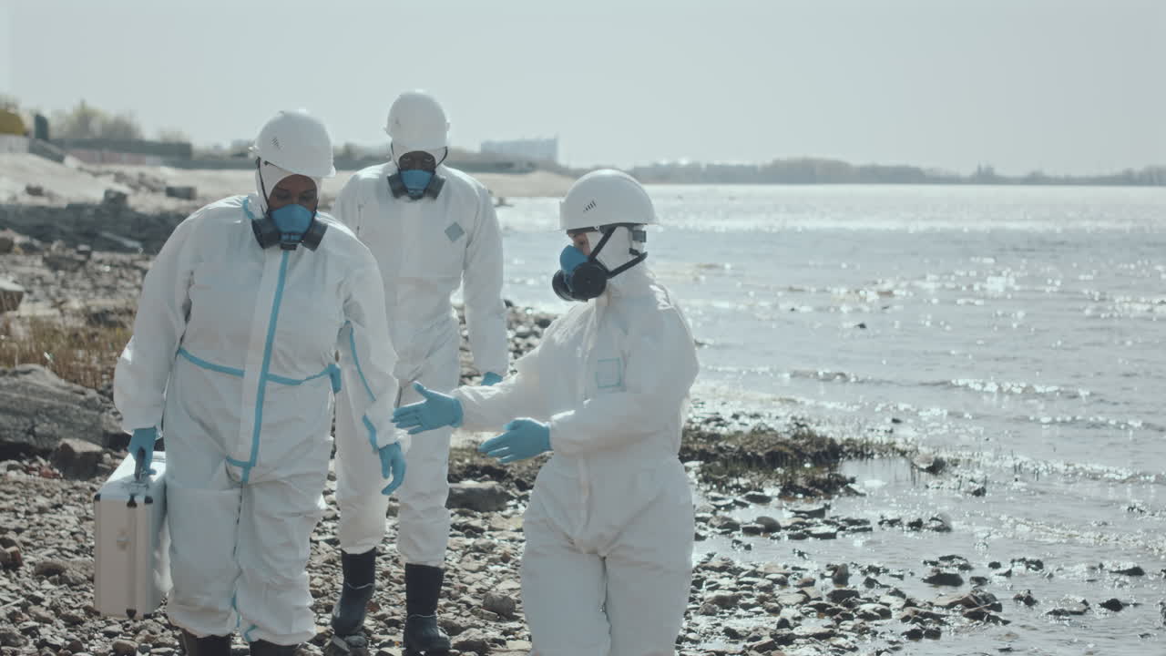Group of Ecologists in Coveralls Walking along Gulf Coast and Talking