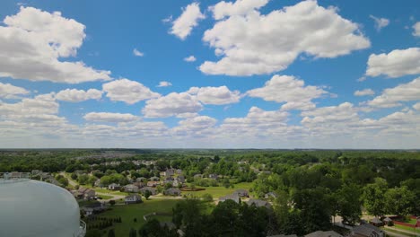 flying past a water tower, revealing a beautiful american suburb on a gorgeous sunny day with fluffy clouds present