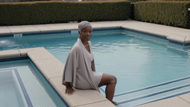 Straightening adult woman turning toward camera on backyard pool coping, wearing swimsuit, cover-up