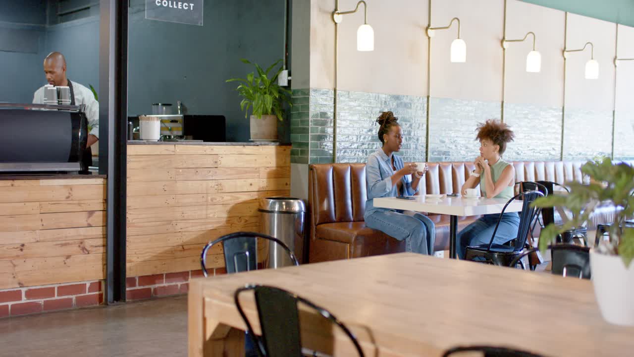 Donne afroamericane che chiacchierano al bancone, sorseggiando e passando una tazza mentre il barista ne posa un'altra al punto di ritiro.
