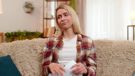 adult woman holds utility bills at home shaking head in frustration due to unexpected high expenses