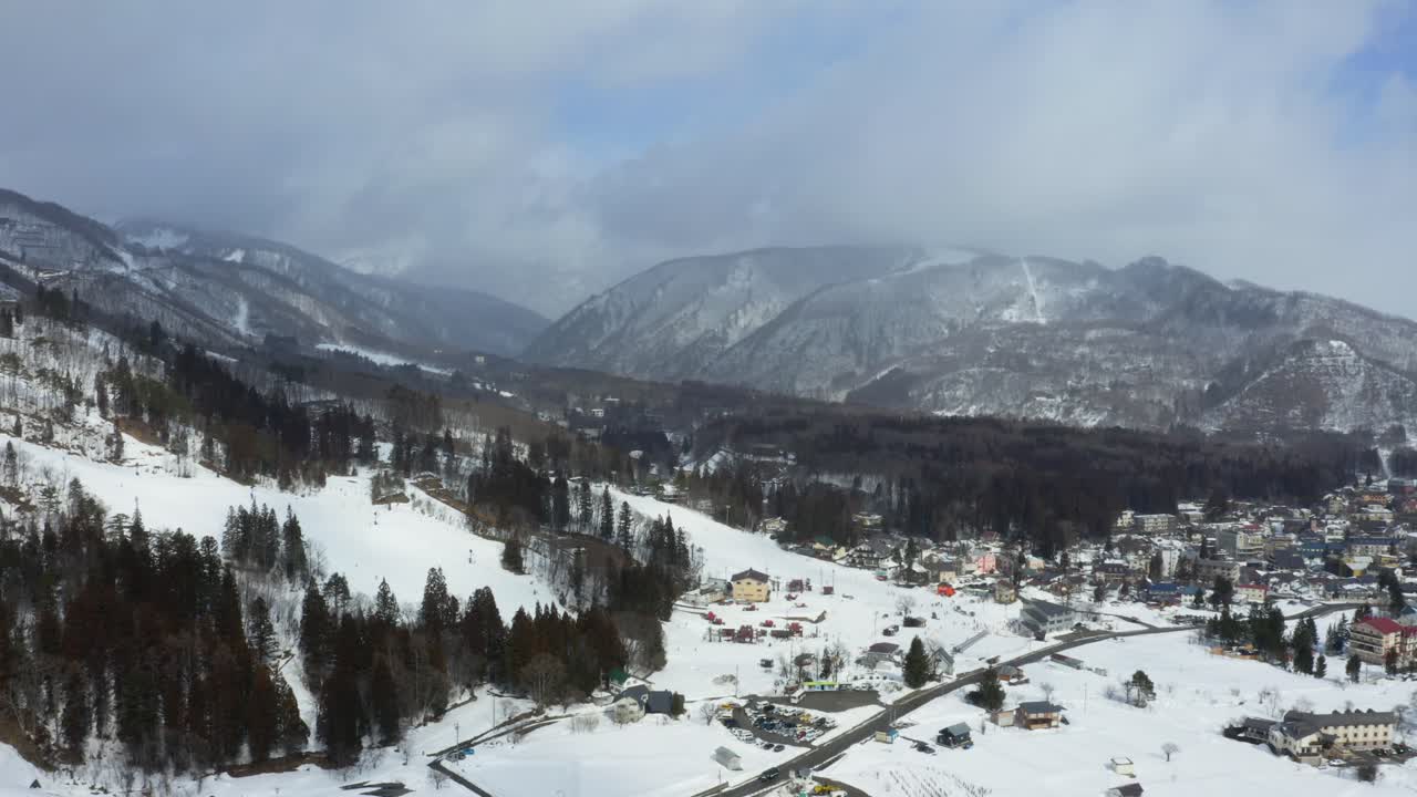 The drone gracefully captures a mesmerizing aerial view of Hakuba valley and it's city in Japan during winter, unveiling a landscape adorned with glistening snow, lush forests, and bustling buildings