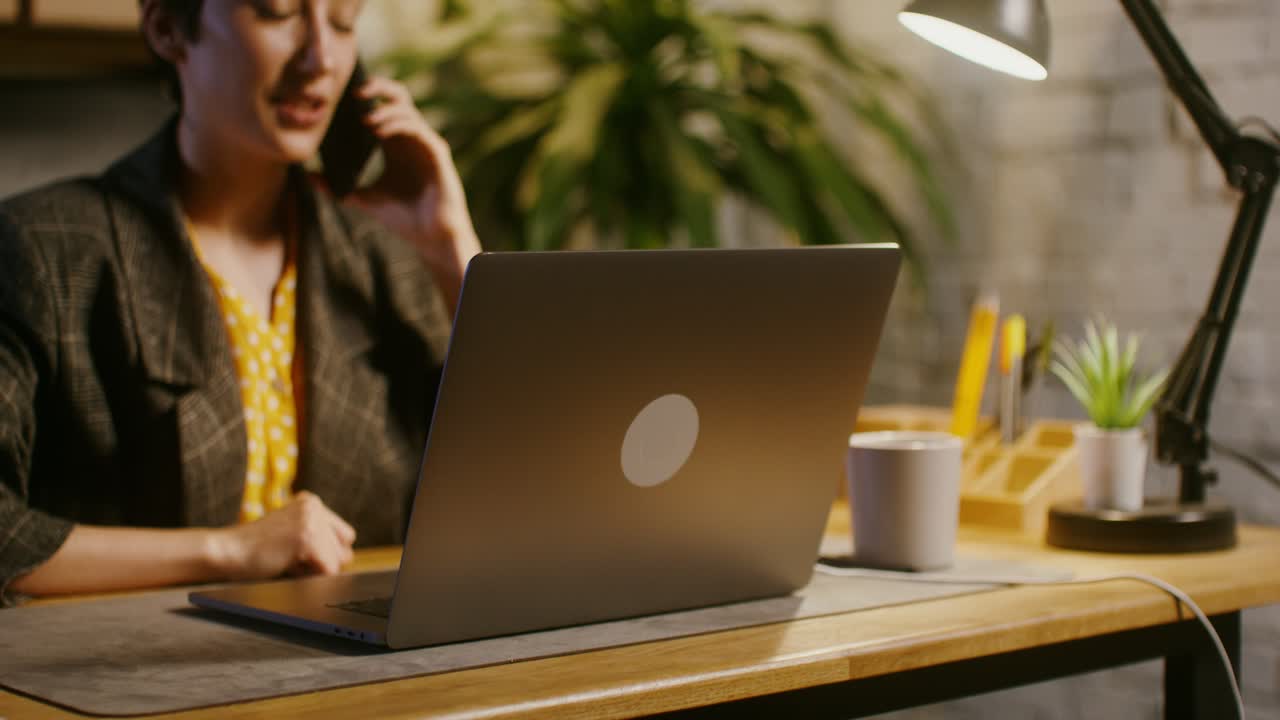 Kvinde arbejder hjemmefra på bærbar computer og taler i telefon