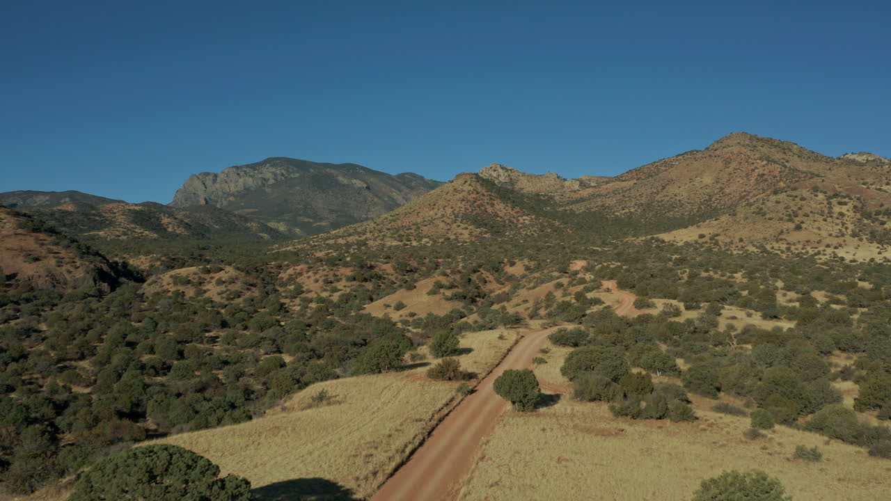 Vista aerea di montagne aride con una strada sterrata e un veicolo fuoristrada, 4K