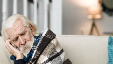 close up portrait of sick man sitting on sofa and having conversation on cellphone