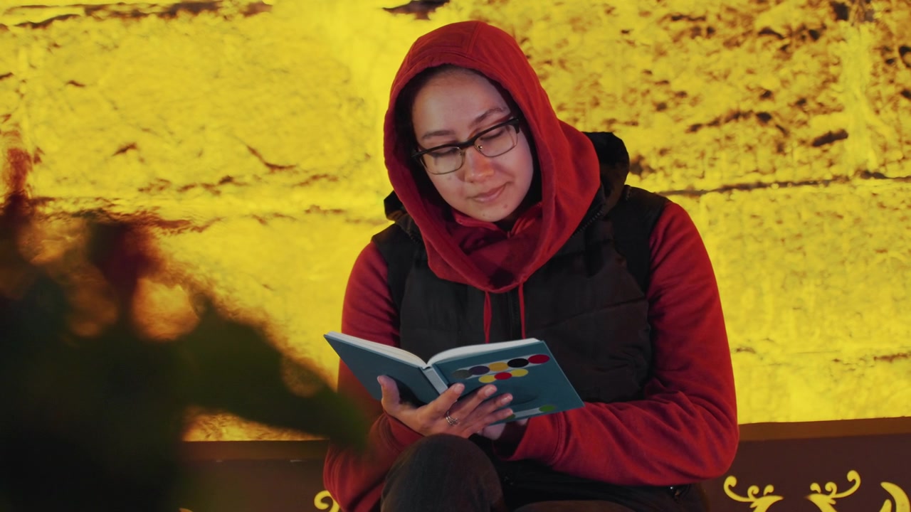 Seorang wanita pendiam menikmati momen membaca buku. Wanita santai berkacamata menikmati malam yang tenang dengan bukunya. Wanita yang tenang diam-diam asyik dalam petualangan buku favoritnya di dekat dinding yang bercahaya lembut.