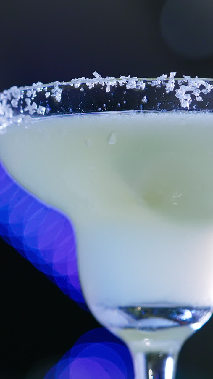 Margarita glass with white beverage. Glass top decorated with crystals of salt. Close up. Blurred backdrop. Vertical video
