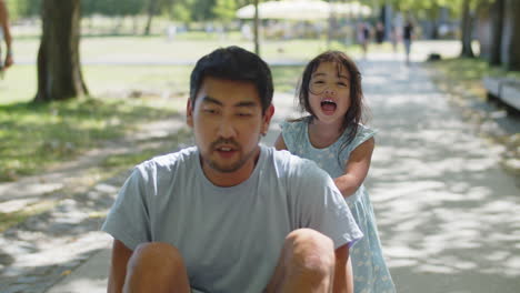 happy asian little girl pushing his father seated on skateboard