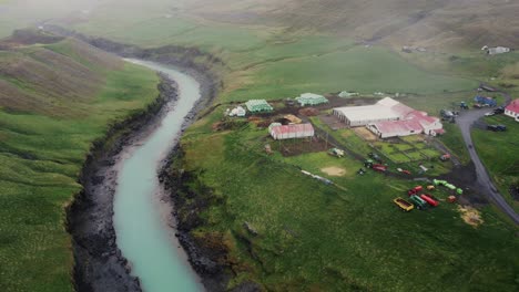 vista aérea de una hermosa granja islandia situada justo encima de un río glacial azul y campos verdes