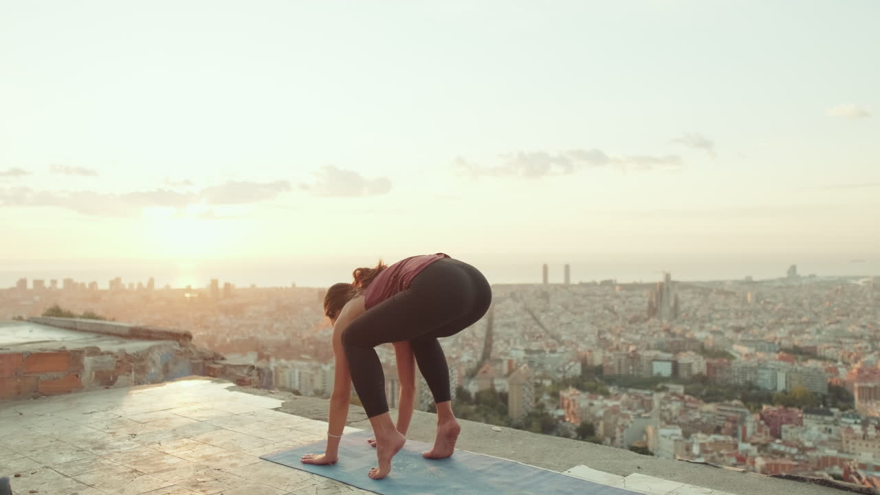 Woman doing yoga on a rooftop overlooking a city at sunrise