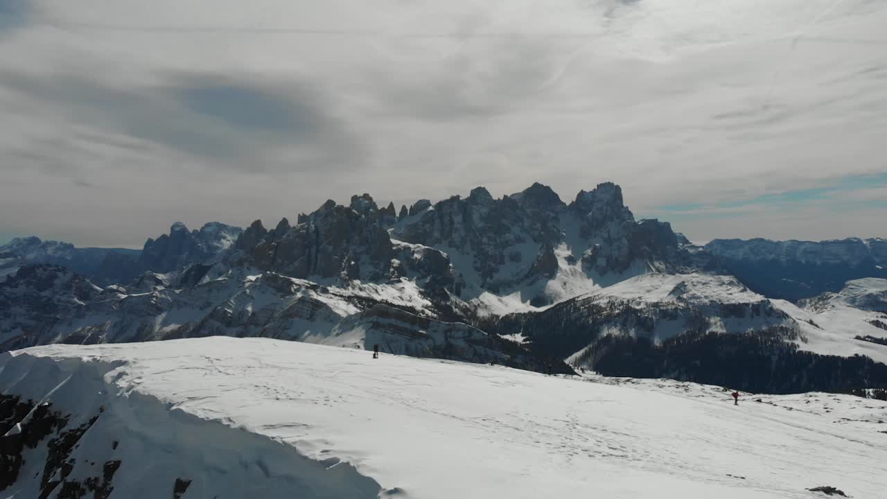 imagen de un dron capturando a un grupo de personas alcanzando el pico cubierto de nieve de la cima jurbrutto, con las impresionantes dolomitas pálidas de san martín proporcionando un telón de fondo impresionante