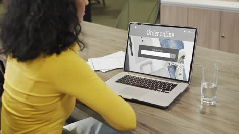 biracial woman at table using laptop, online shopping for clothes and accessories, slow motion