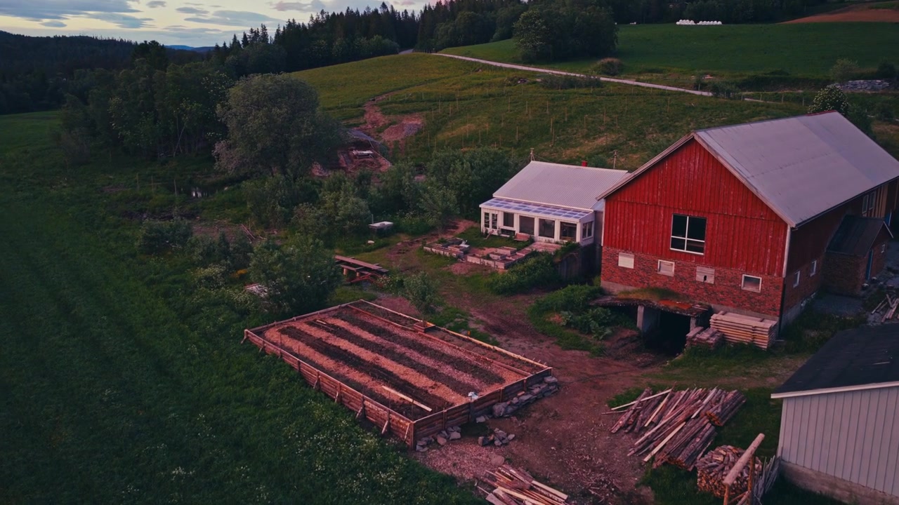 Højbedshave nær en lade og et drivhus i landlige omgivelser med omgivende vegetation. Luftfoto med drone