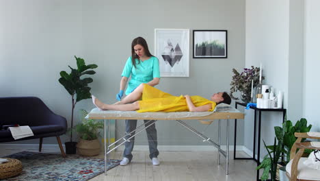 two girls in a beauty salon master in a bathrobe and gloves doing the procedure to remove hair on the legs with a sugar mixture