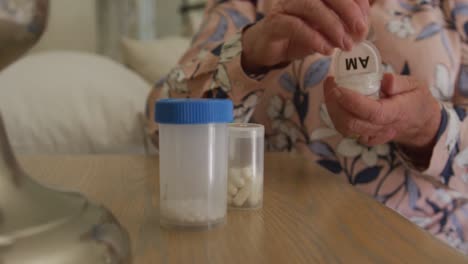 sección media de una mujer mayor caucásica que saca píldoras de contenedores medicinales en casa