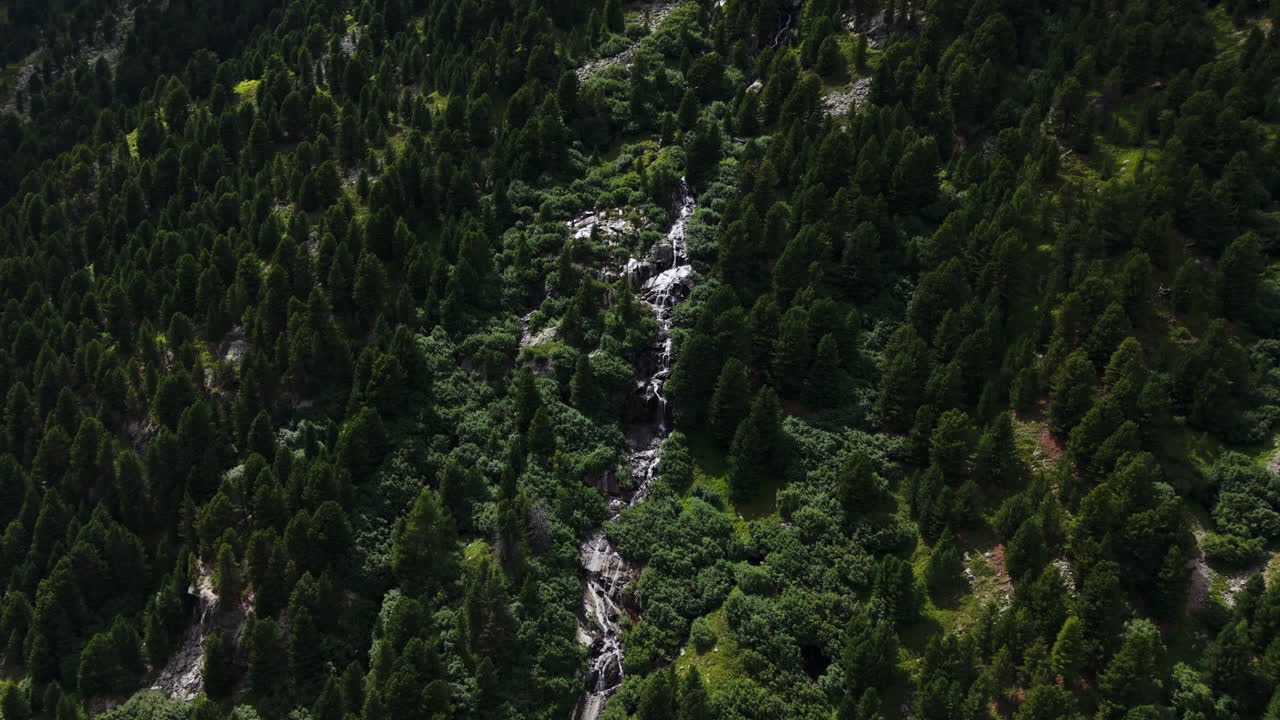 Drone pans sideways along a mountain slope, following a winding river flowing between dense green trees