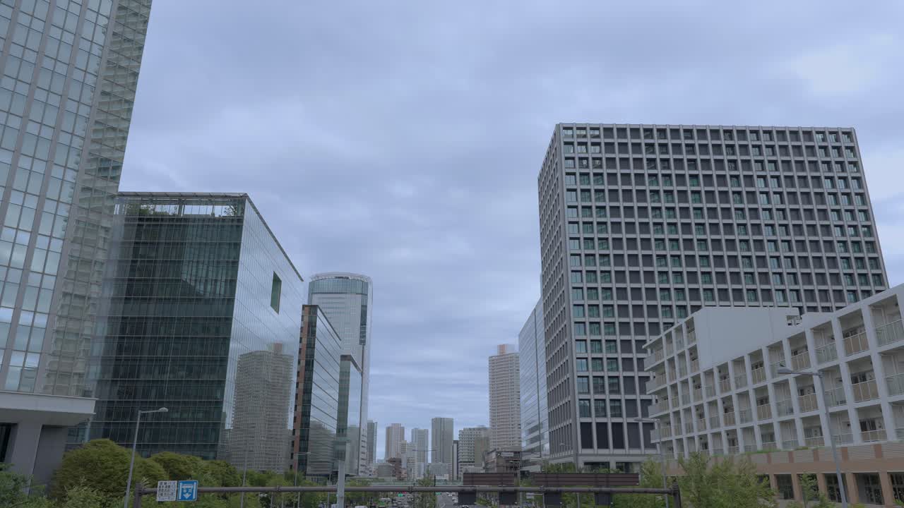 A low-angle shot of modern glass skyscrapers and buildings in Tokyo's Toyosu area against an overcast sky