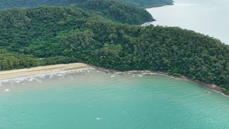 aerial footage glides over lush rainforest meeting turquoise sea along a remote coastline. natural daylight, smooth drone movement, and expansive landscape views dominate the scene