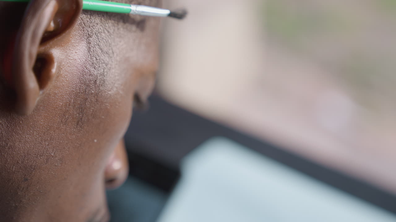 Rear view black paintbrush behind ear, observer looking toward tablet, soft bokeh background, warm sunlight on skin, quiet pause between strokes, thoughtful rhythm, serene urban workshop vibe