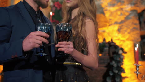 loving couple drinks red wine from large glasses in room decorated for holidays. nice evening clothes.