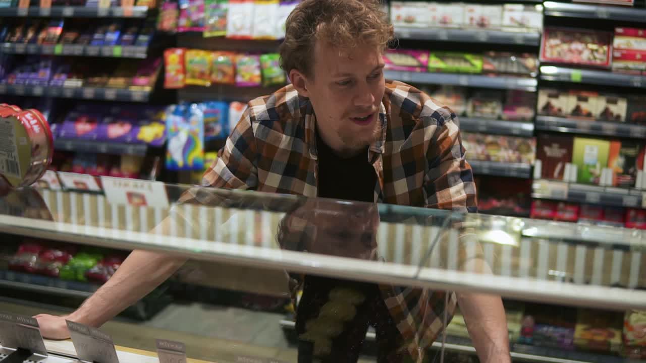 매장에서 쇼핑하는 동안 제품을 검색하는 유리 쇼케이스를 보는 카우카시안 남자의 초상화. 쇼케이스를 쳐다보고 특정 제품을 가리키는 느린 동작