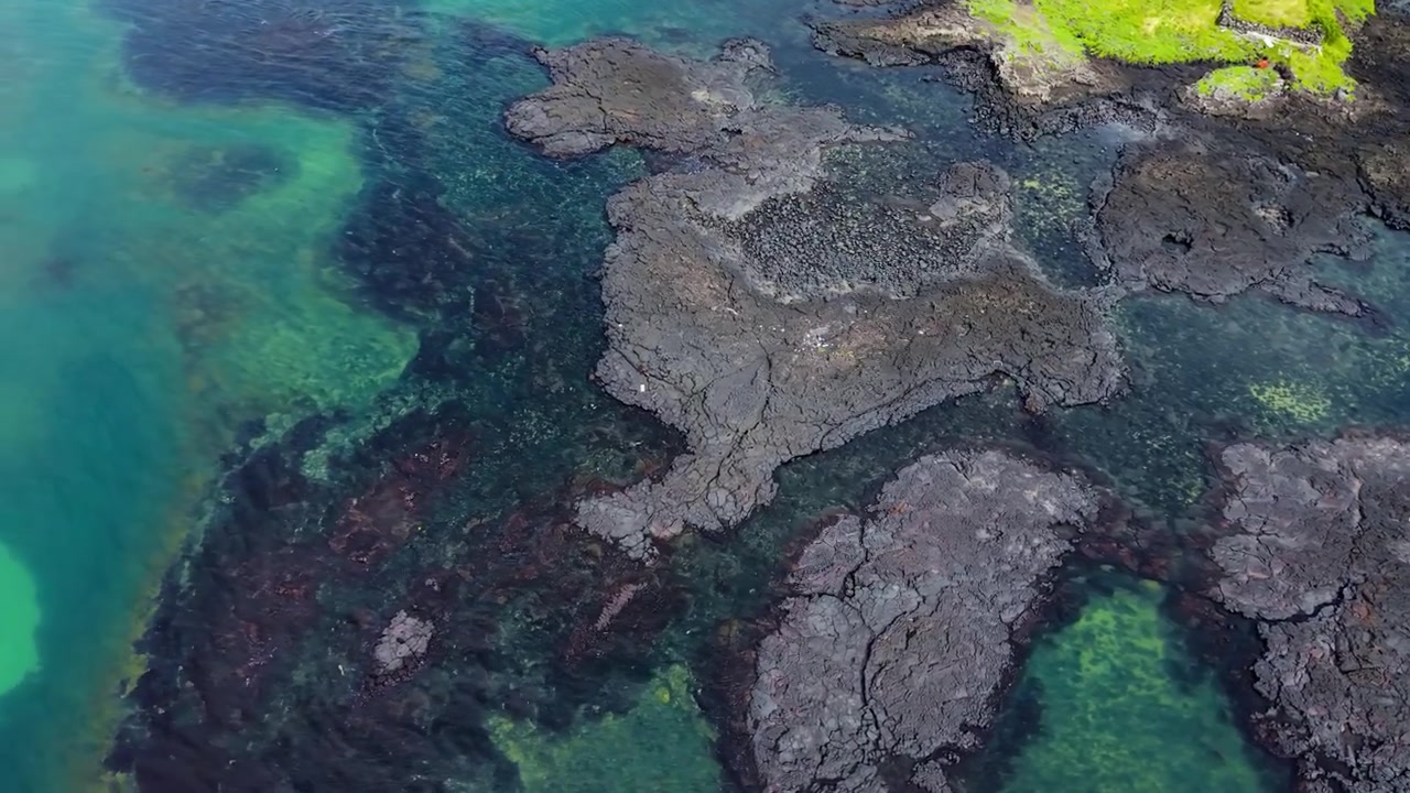 Aerial orbiting view of volcanic lava rocks and tidal pools along the coastline of Singgyemul Park, Jeju Island, with crystal clear turquoise water