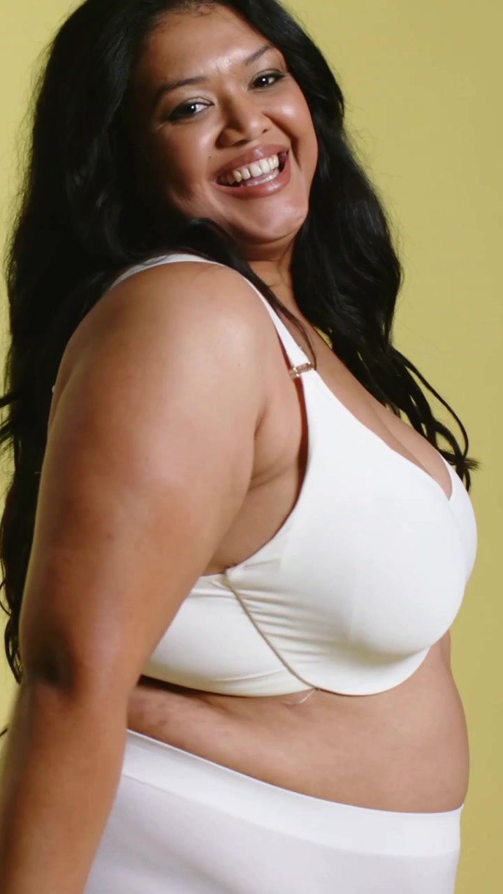 Video verticale: Modella sorridente che posa e si gira in studio, indossando un reggiseno bianco e biancheria intima a vita alta