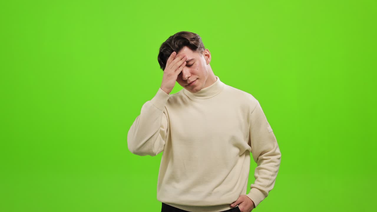 L'uomo è in piedi e guarda la telecamera. Si tiene una mano sulla fronte. È deluso. È in piedi su uno sfondo verde. Schermo verde. 4K.