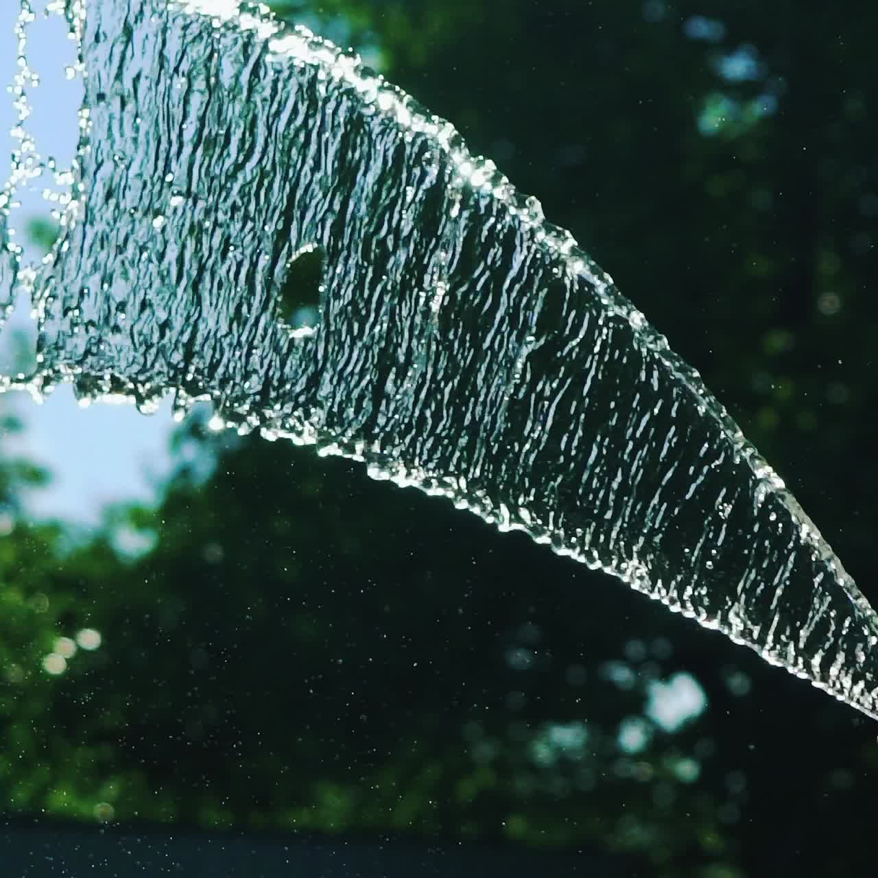 Stream of water spraying from garden hose, close up. Watering the green grass. Slow Motion.