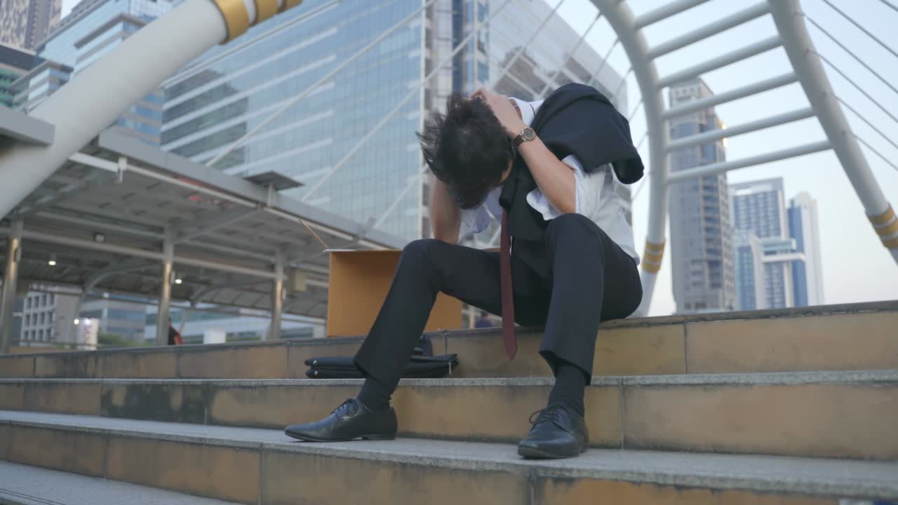 Asian business man feeling sad after unemployment from his company. The man sitting outdoor feeling stress worry about losing the job due to world economic problem from covid 19 crisis concept.
