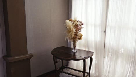 vase with assorted flowers on a table in a room filled with white light