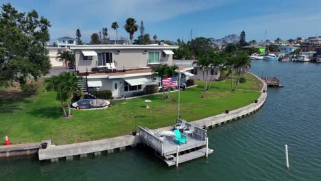 american flag on private jetty of apartment building at john pass river in florida. surfboard in garden and tropical palm trees. aerial backwards wide shot. proud family in madeira beach.