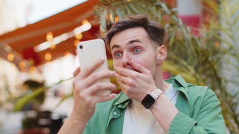 excited happy winner man using smartphone looking amazed at screen celebrating win good message news