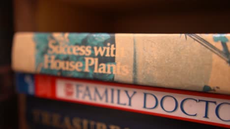 a closeup truck pan tracking down the spine of two household nonfiction books stacked on a bookshelf about plants and family healthcare