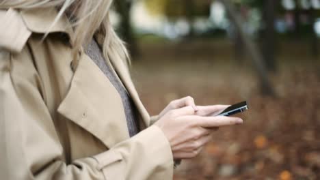 Cerca-De-Una-Mujer-Escribiendo-Un-Mensaje-En-Un-Teléfono-Celular-En-Un-Parque-De-Otoño
