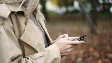 close up of a woman writing message on cell phone in a autumn park