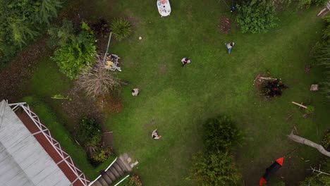 aerial top down of friends playing with toy and throwing on grass field in garden. happy people enjoying holidays. circling shot.