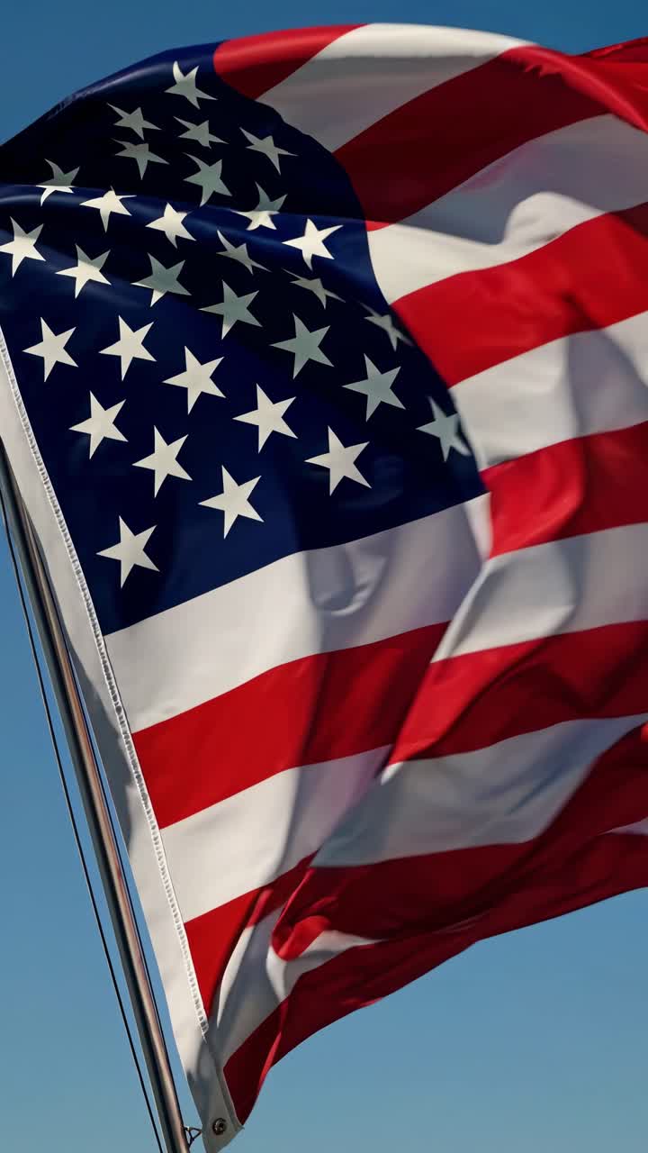 Bandiera americana che sventola con grazia nel vento contro un cielo blu vibrante, simboleggiando gli ideali di libertà e democrazia e incarnando al contempo l'orgoglio e l'identità nazionale